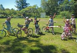 Six children, balancing on bicycles, pose with hands raised