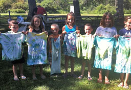 Seven children pose with tee shirts they've tie dyed at Camp Eaton.