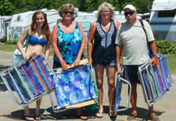 A teenaged girl, two woman and a man head to the beach with lounge chairs